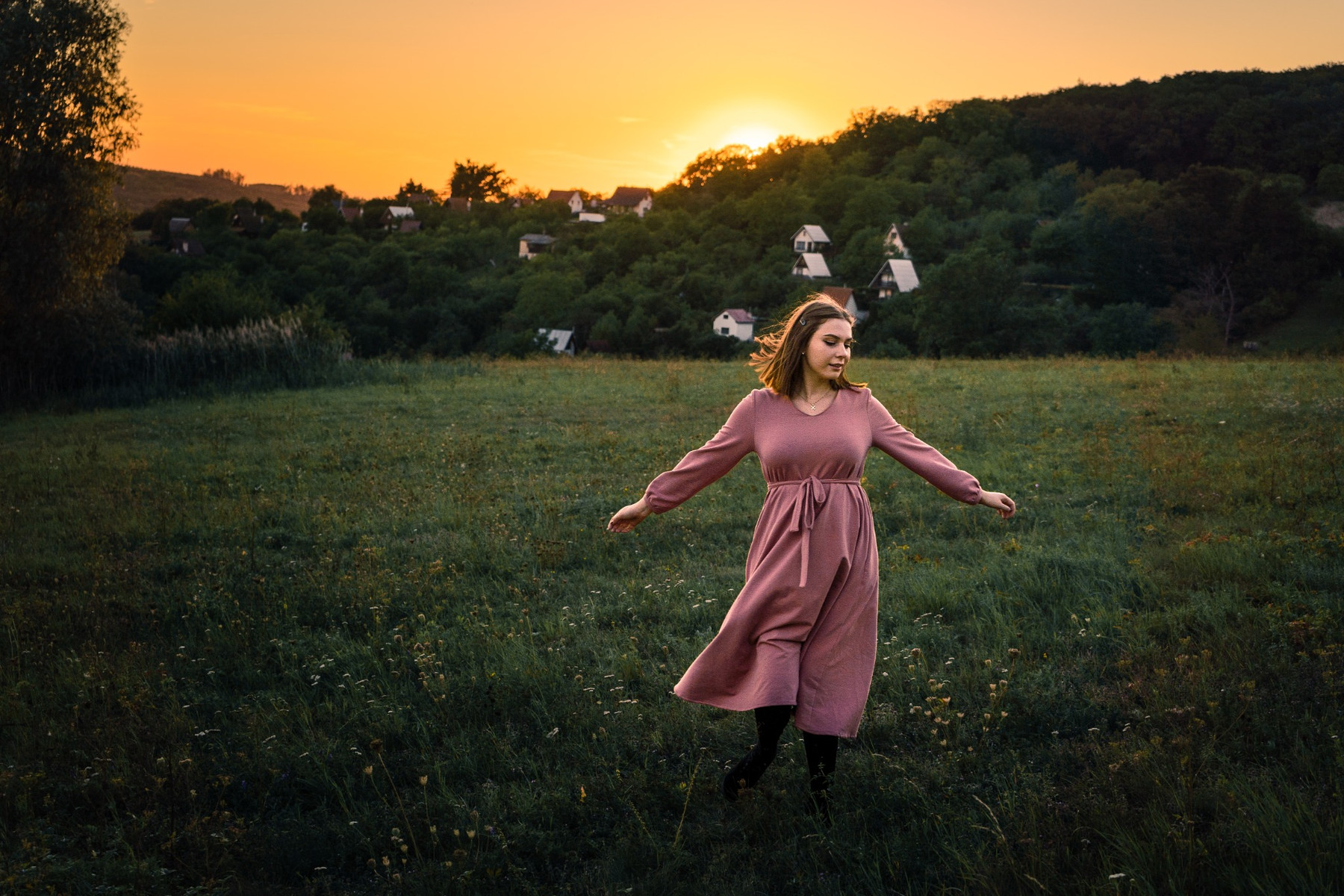 Portrait extérieur d'une femme en robe rose dans une prairie au coucher du soleil